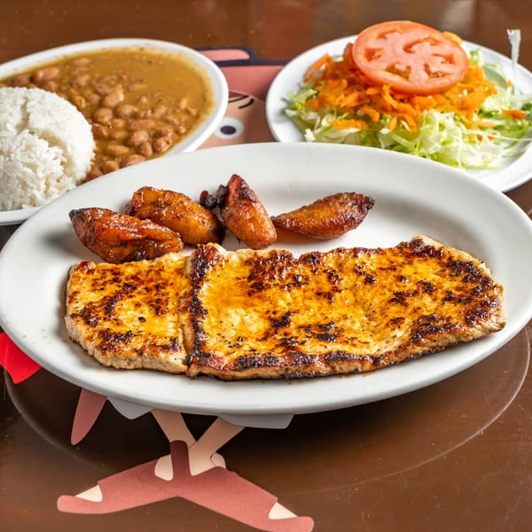 Grilled pork loin with fried plantains, rice, beans, and a side salad at Los Arrieros.