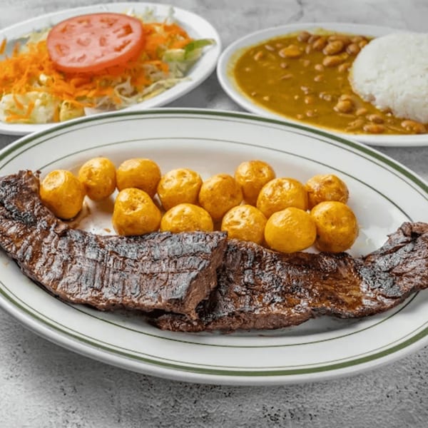 Colombian skirt steak with small yellow potatoes, a side salad, and a bowl of beans and rice.