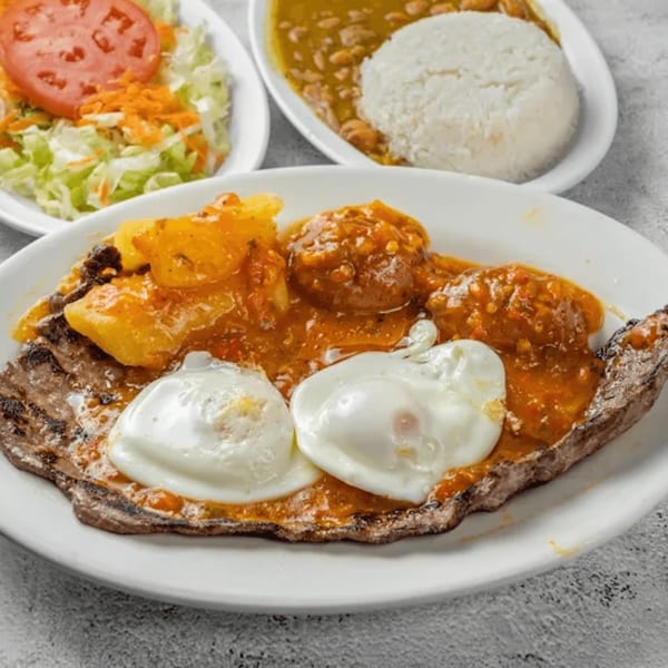 Colombian grilled steak with two fried eggs, potatoes, beans, rice, and a side salad.