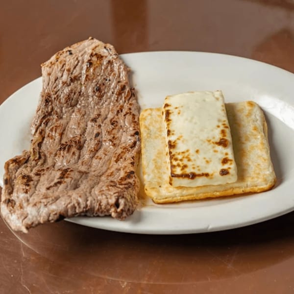 Grilled steak and two pieces of white cheese on a white plate at Los Arrieros Restaurant.