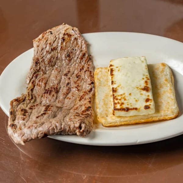 Grilled steak and two pieces of fried cheese on a white plate from Los Arrieros Restaurant.