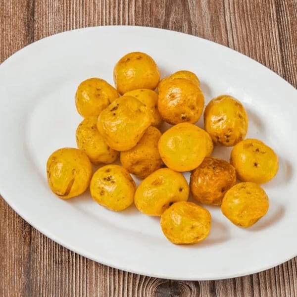 A white oval plate filled with small, golden-yellow Colombian papas criollas on a wooden table.