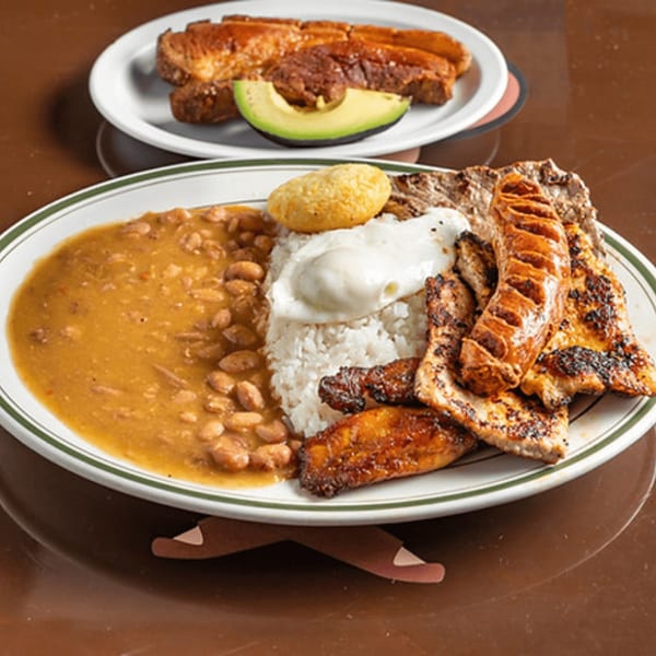 A Colombian bandeja paisa with beans, rice, fried egg, sausage, grilled meat, and plantains.